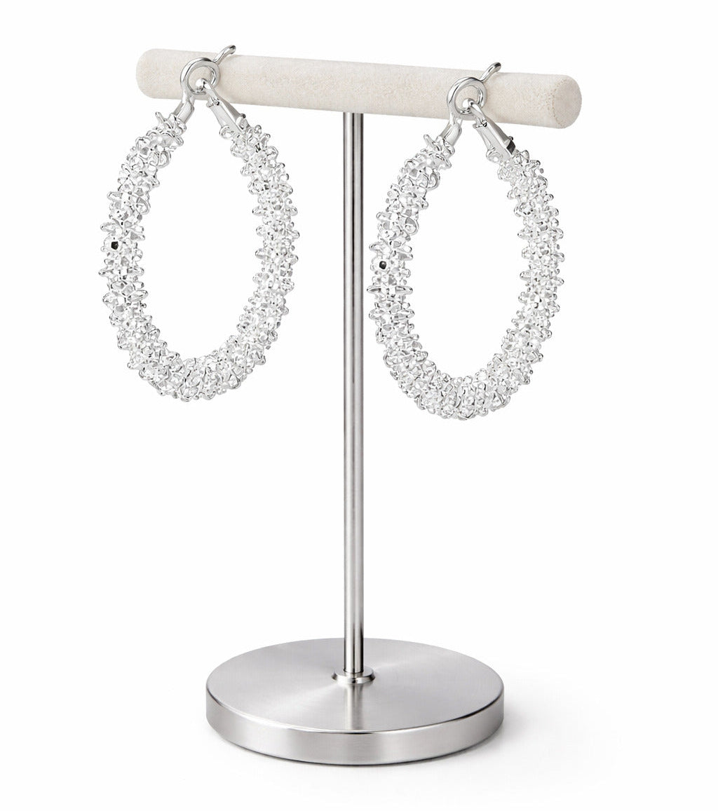 Pair of silver hoop earrings on a white stand against a white background