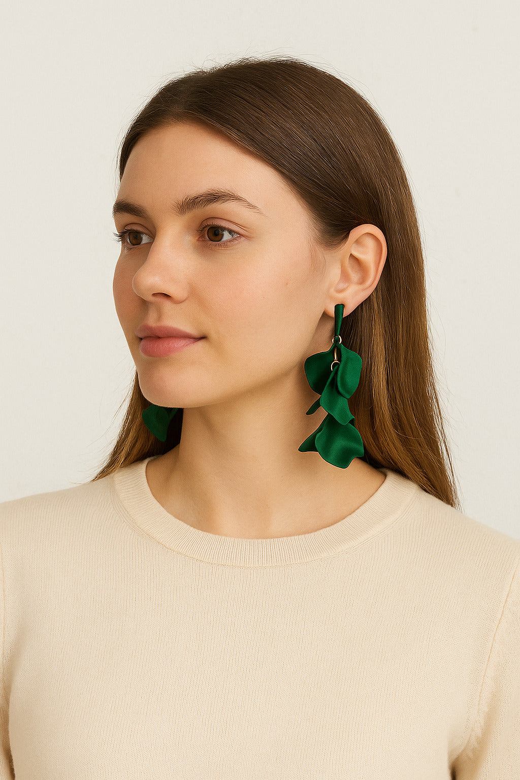 Woman wearing green leaf-shaped earrings against a plain background
