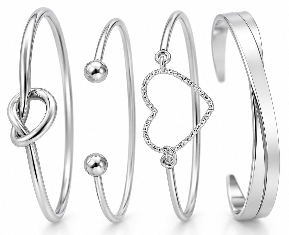 Four silver-toned open cuff bracelets with different designs, including a heart-shaped link, a knot, two small beads, and a smooth twisted band, displayed on a white background.