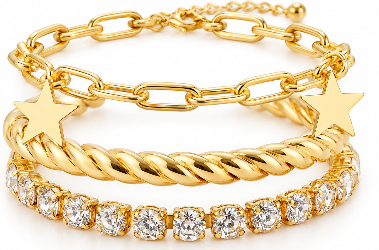 A stack of three gold bracelets on a white background: a paperclip chain bracelet, a twisted rope bracelet with a star charm, and a tennis bracelet with clear round stones.