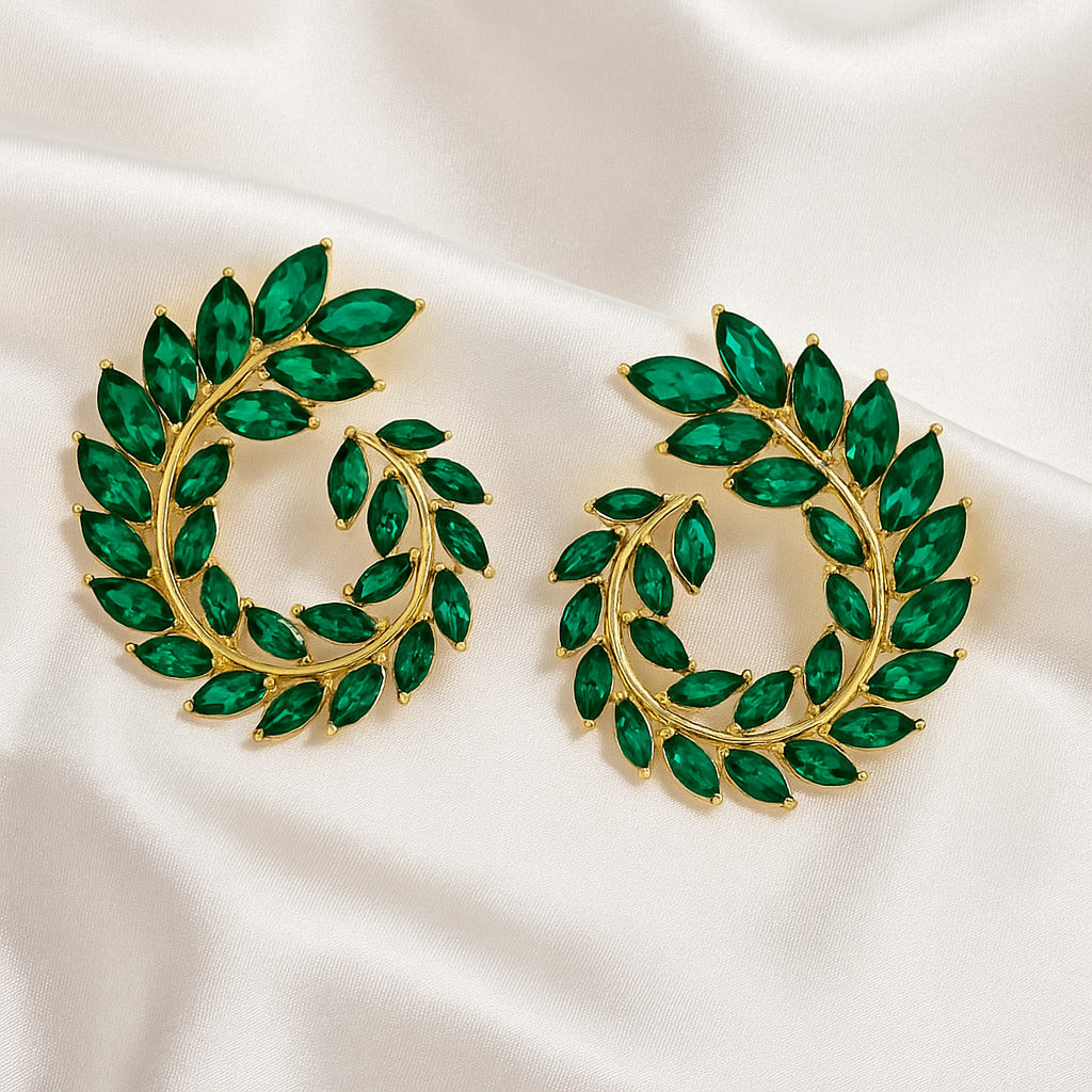 Gold earrings with green gemstones on a white satin background