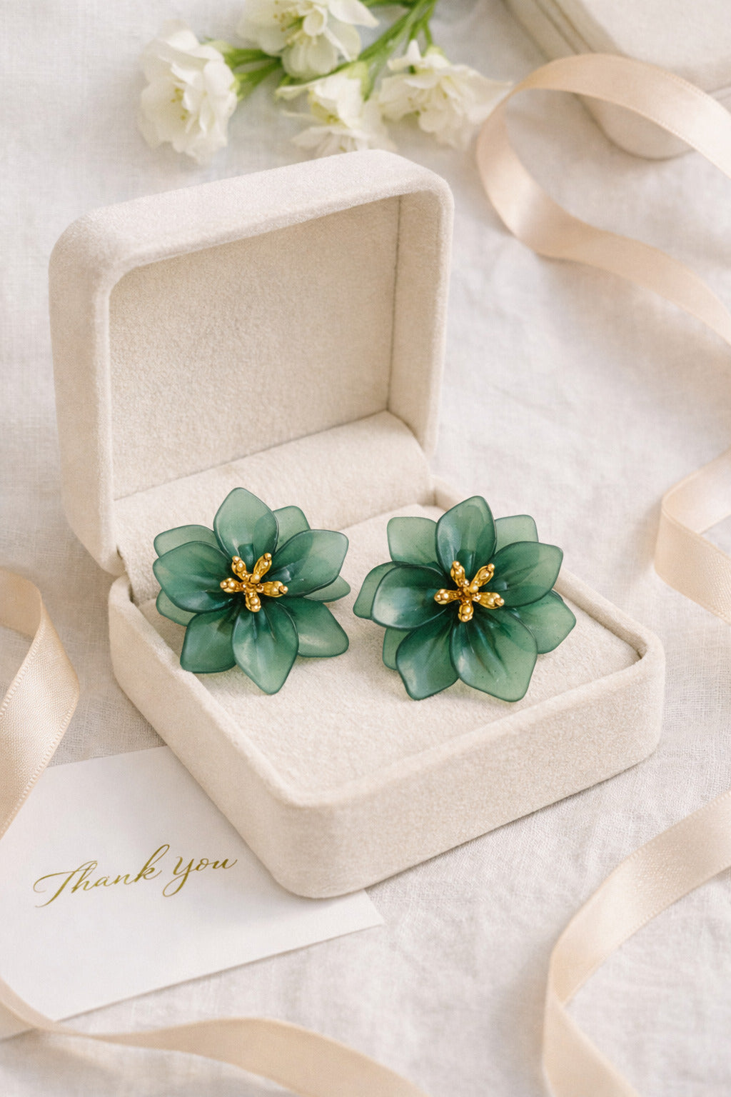 Green floral earrings in a jewelry box with ribbons and flowers in the background