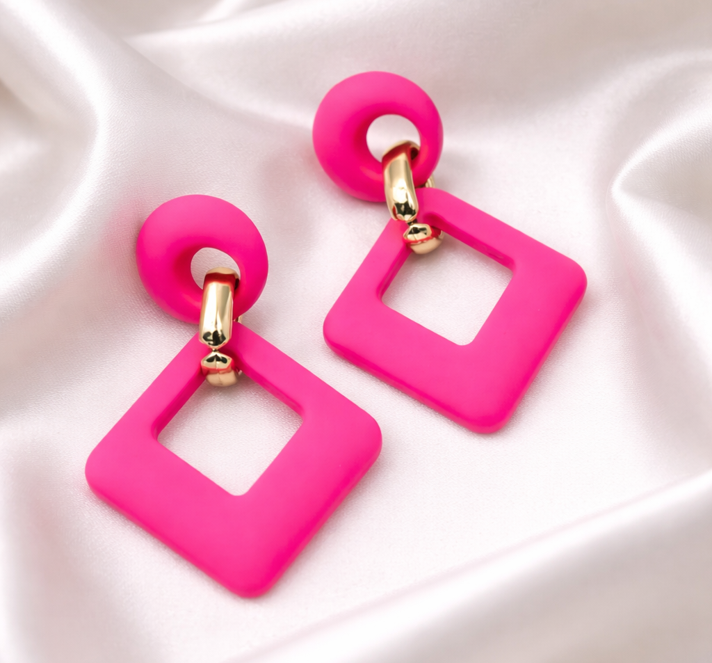 Pink square earrings with gold accents on a white fabric background