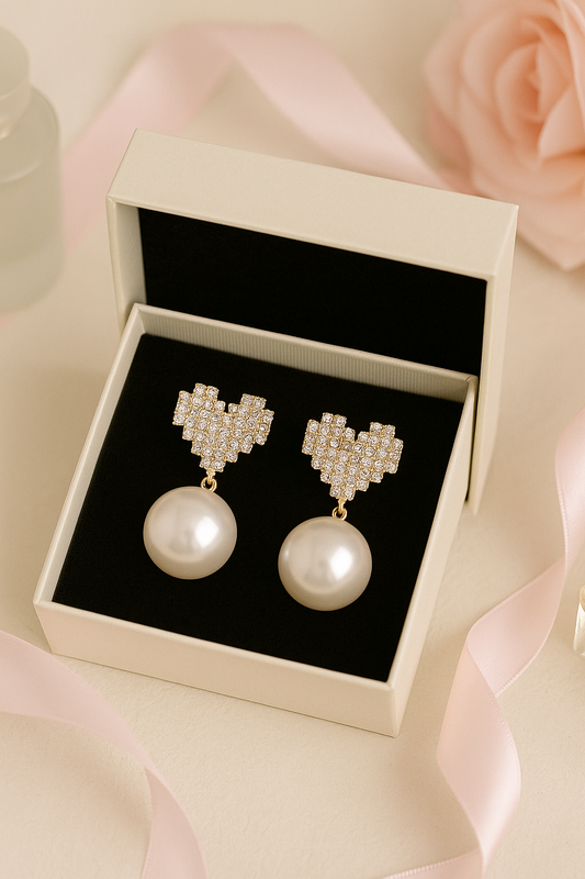Pearl earrings with heart-shaped designs in a box on a soft pink background