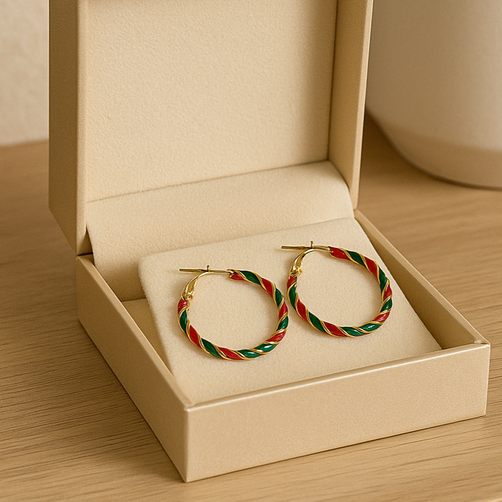 Pair of gold hoop earrings with red and green accents in a beige jewelry box on a wooden surface.