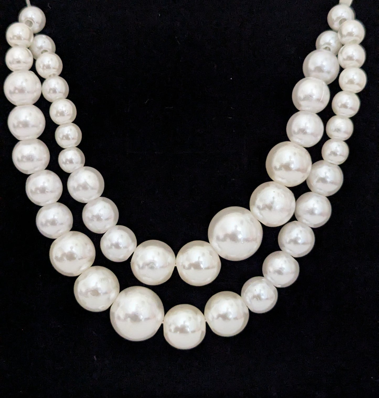 Two strands of white pearls on a black background