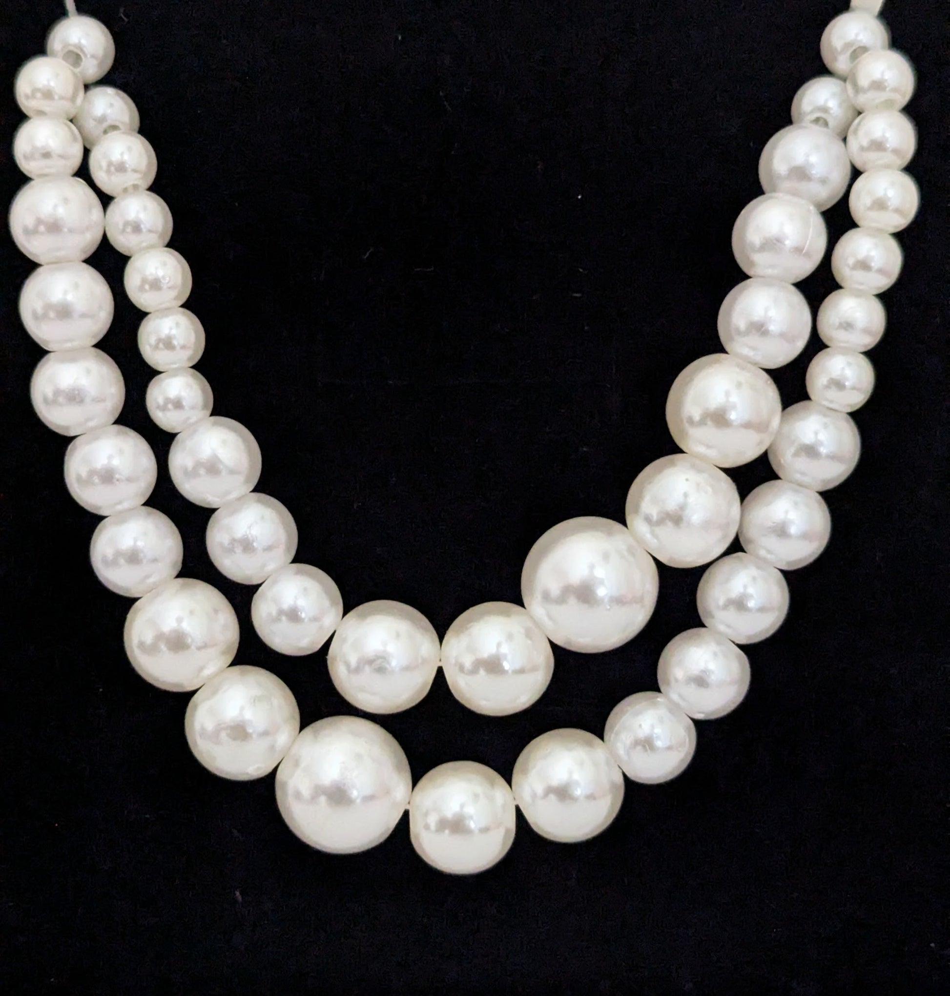 Two strands of white pearls on a black background