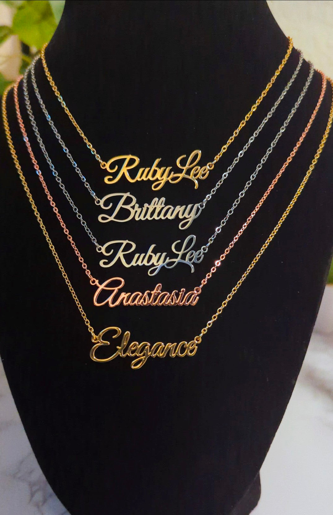 Gold nameplate necklaces on a black mannequin bust with names engraved.