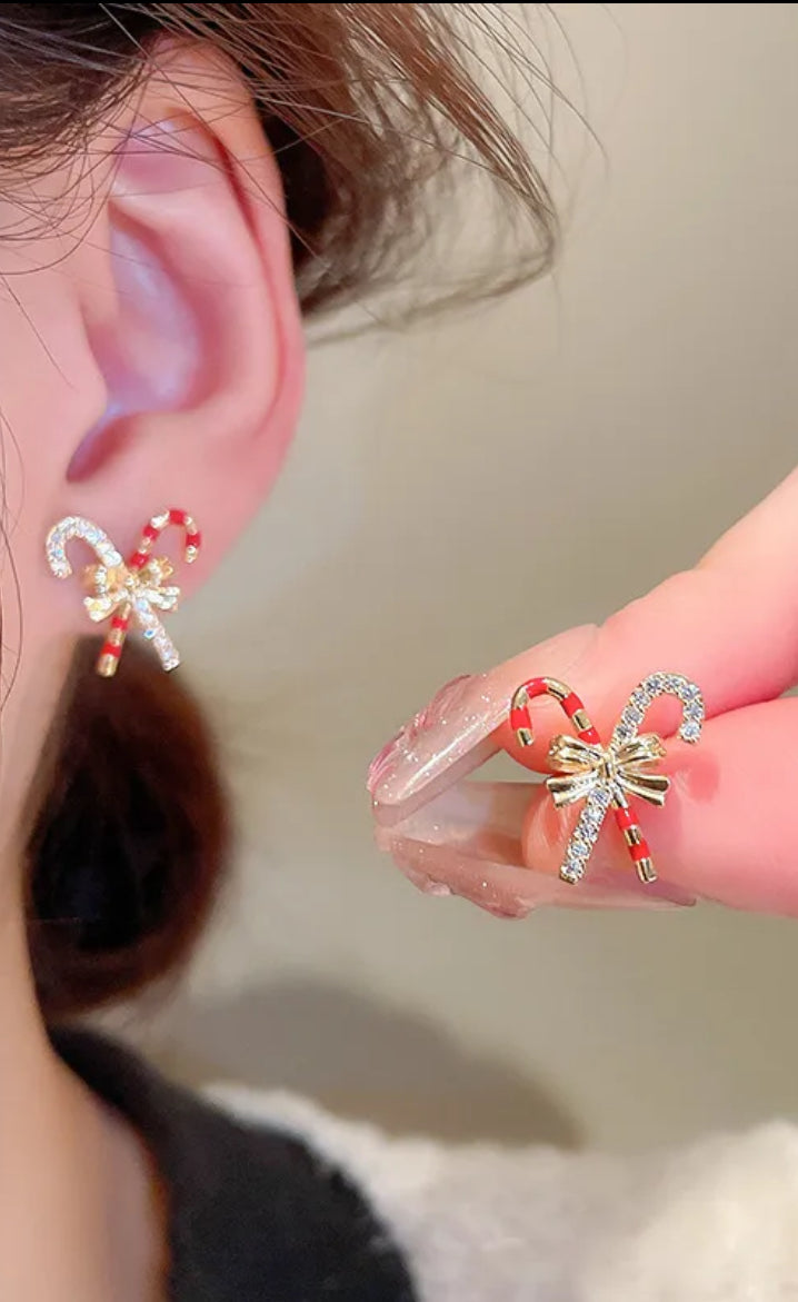 Close-up of a person wearing festive-themed earrings with candy cane and snowflake designs.