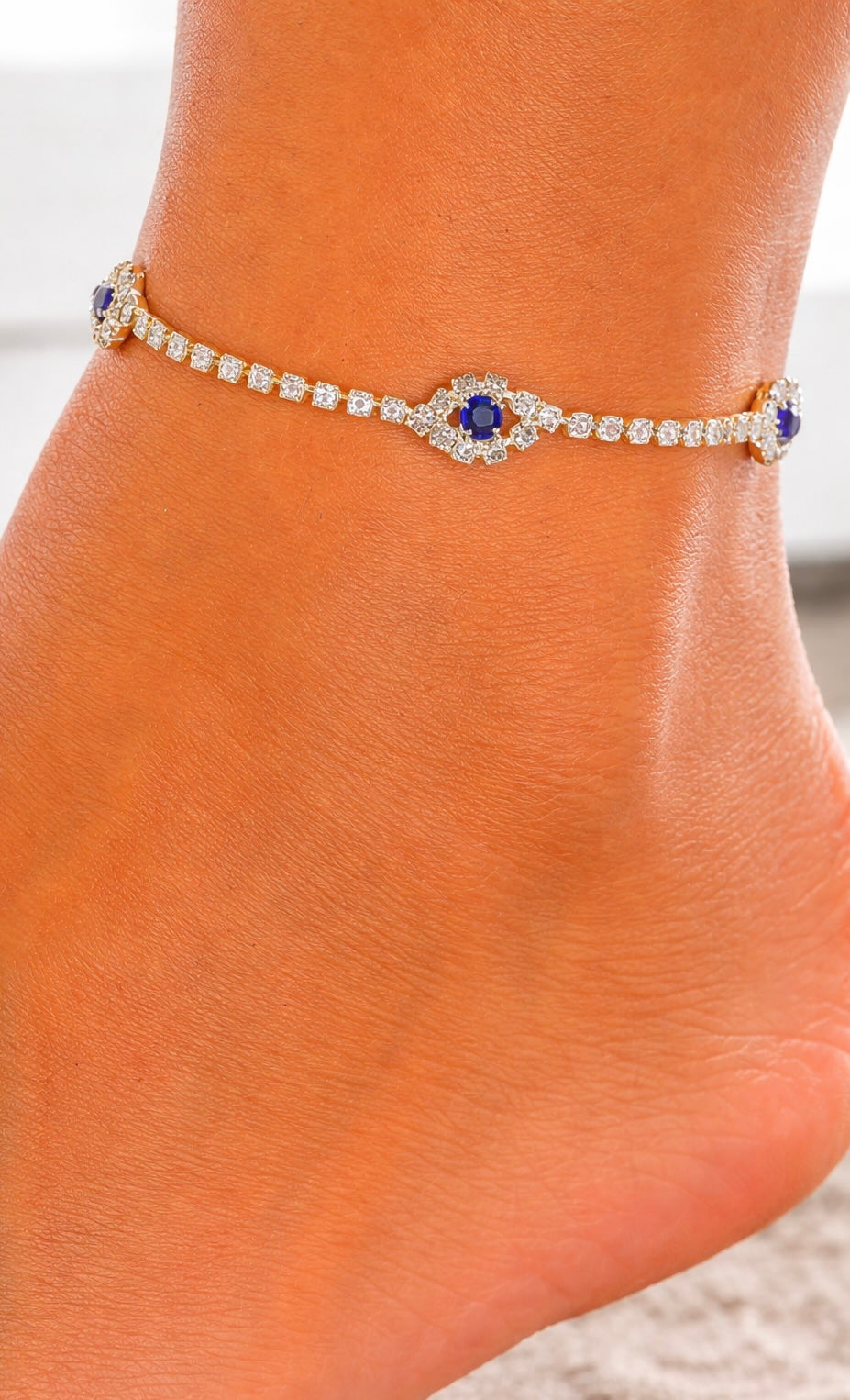 Ankle bracelet with a blue gemstone on a person's ankle against a neutral background