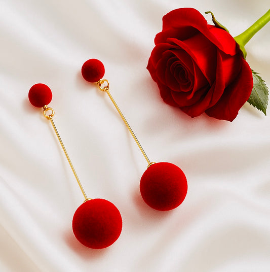 Red ball earrings with gold stems next to a red rose on a white background