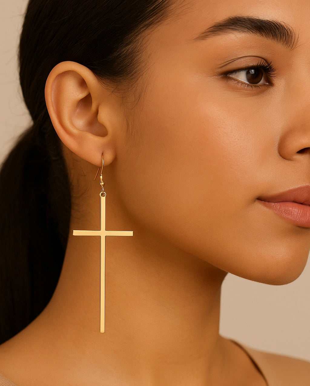 Gold cross earring worn by a model against a neutral background