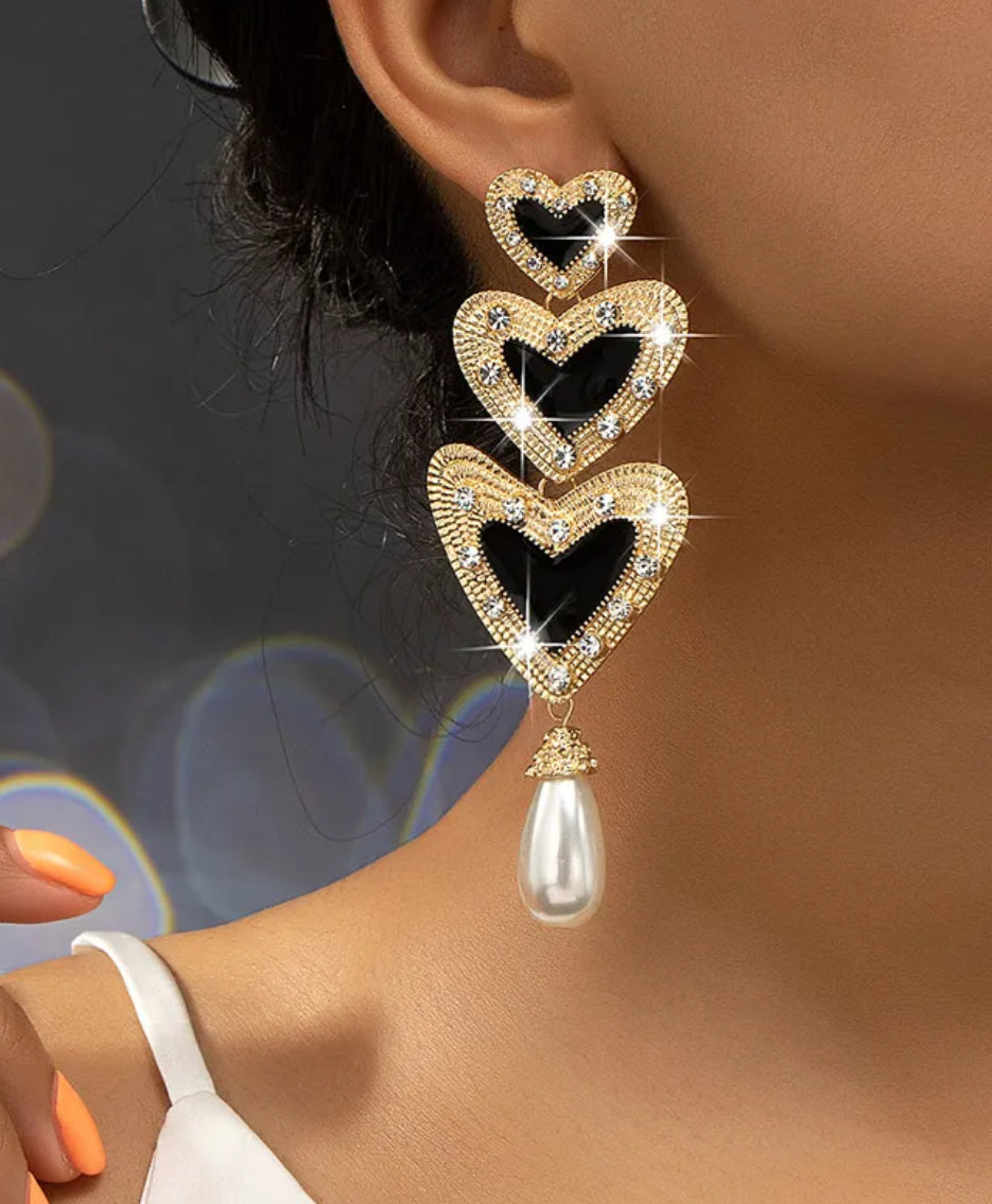 Heart-shaped earrings with a pearl drop worn by a person against a blurred background