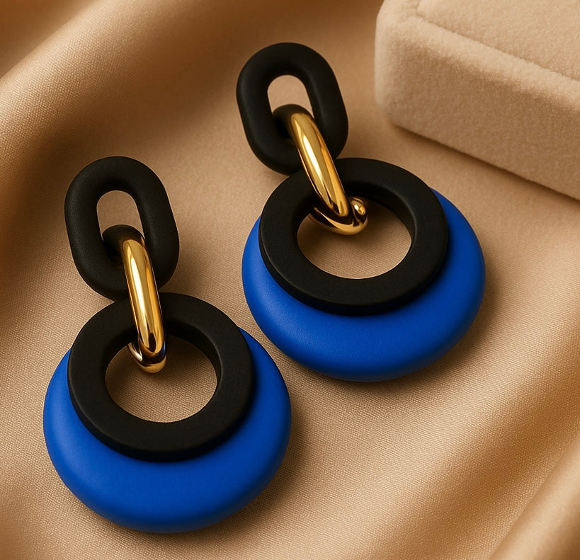 Pair of earrings with black and blue circular design on a beige fabric background