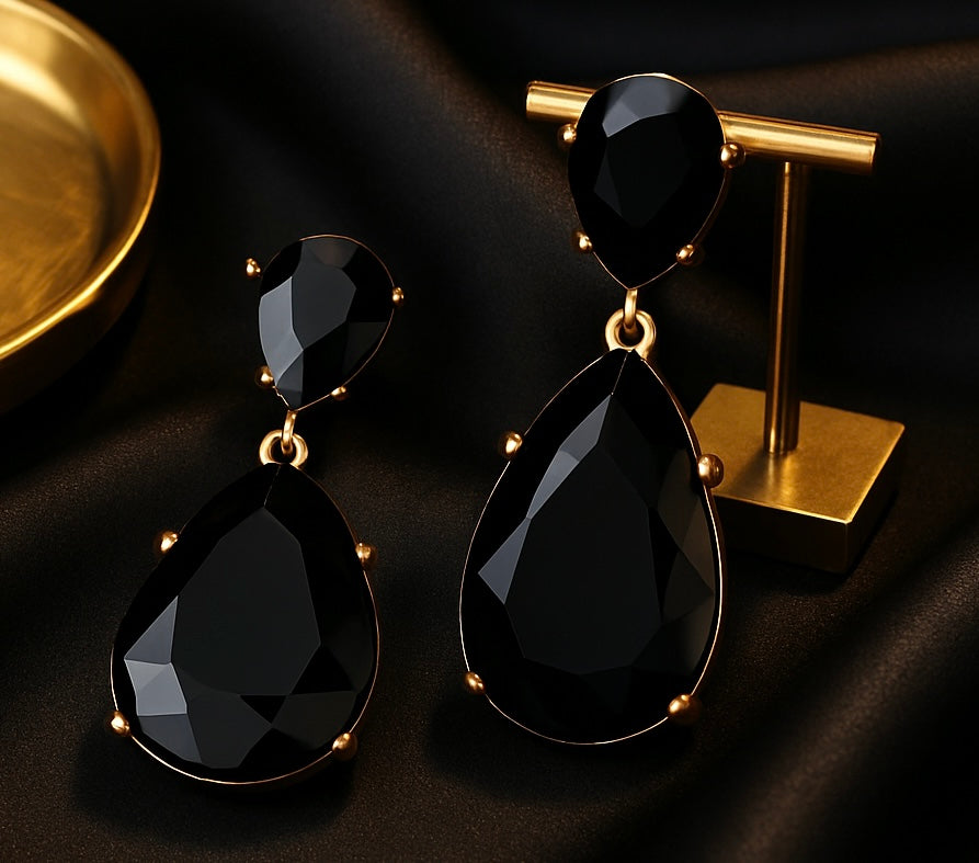 Black teardrop earrings on a gold stand against a dark background