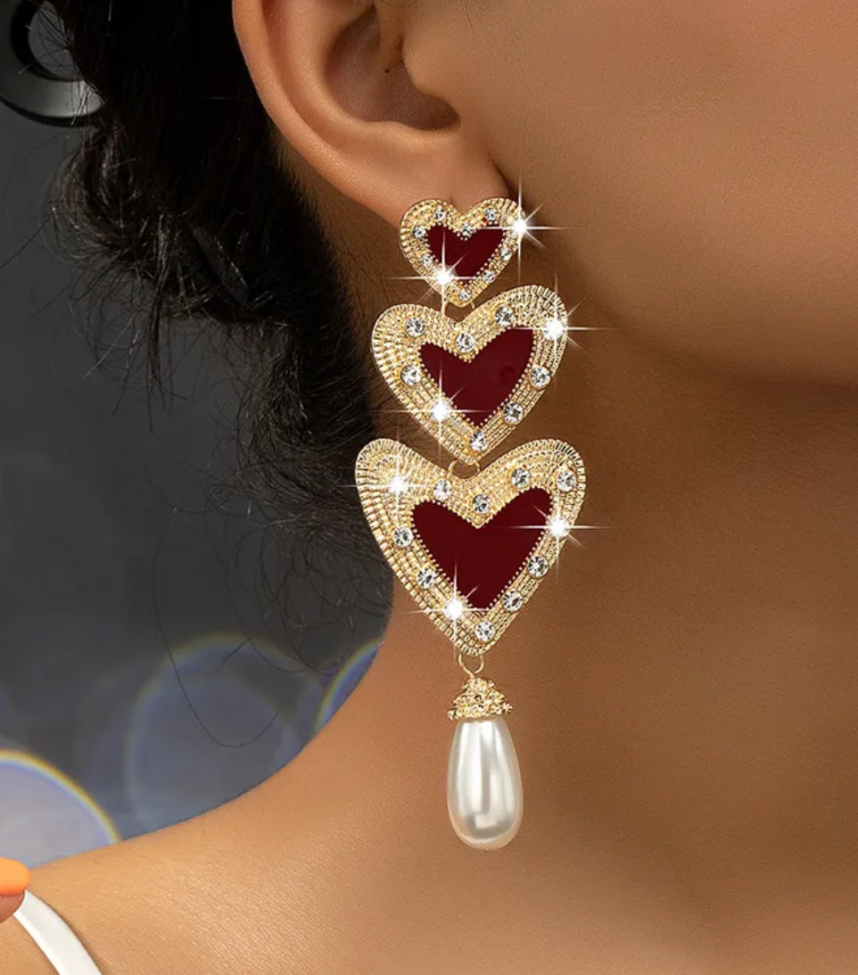 Heart-shaped earrings with a pearl drop worn by a person against a blurred background