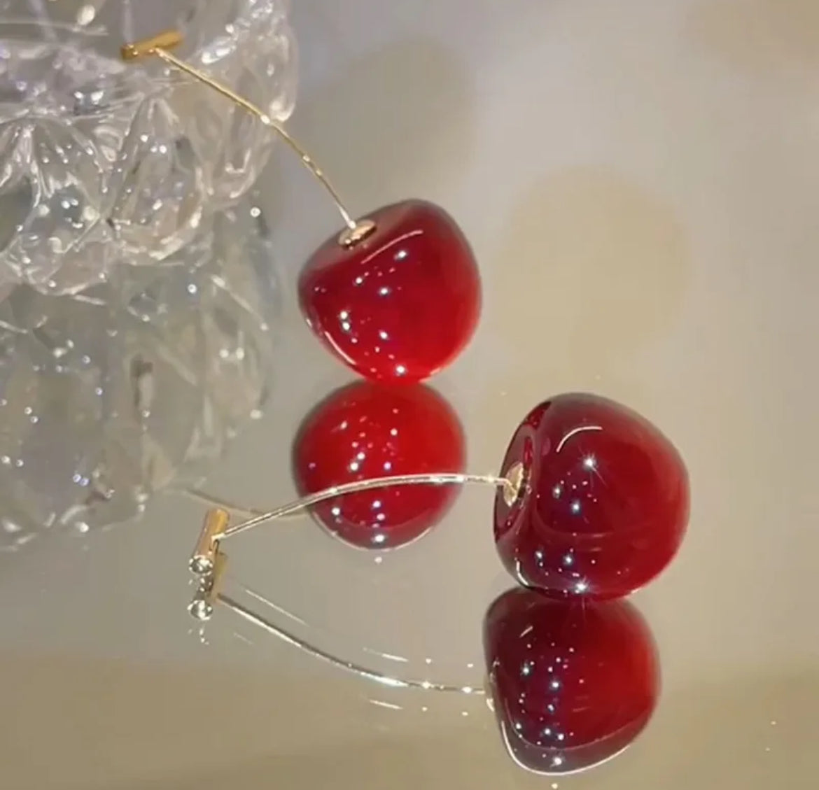 Red cherries with gold stems on a reflective surface