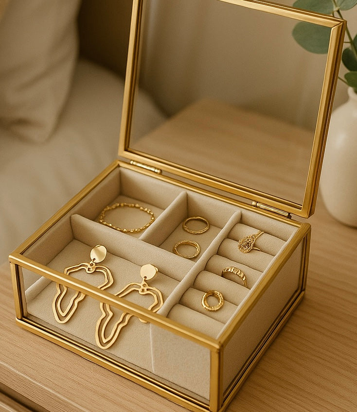 Gold jewelry box with compartments for earrings and rings on a wooden surface.