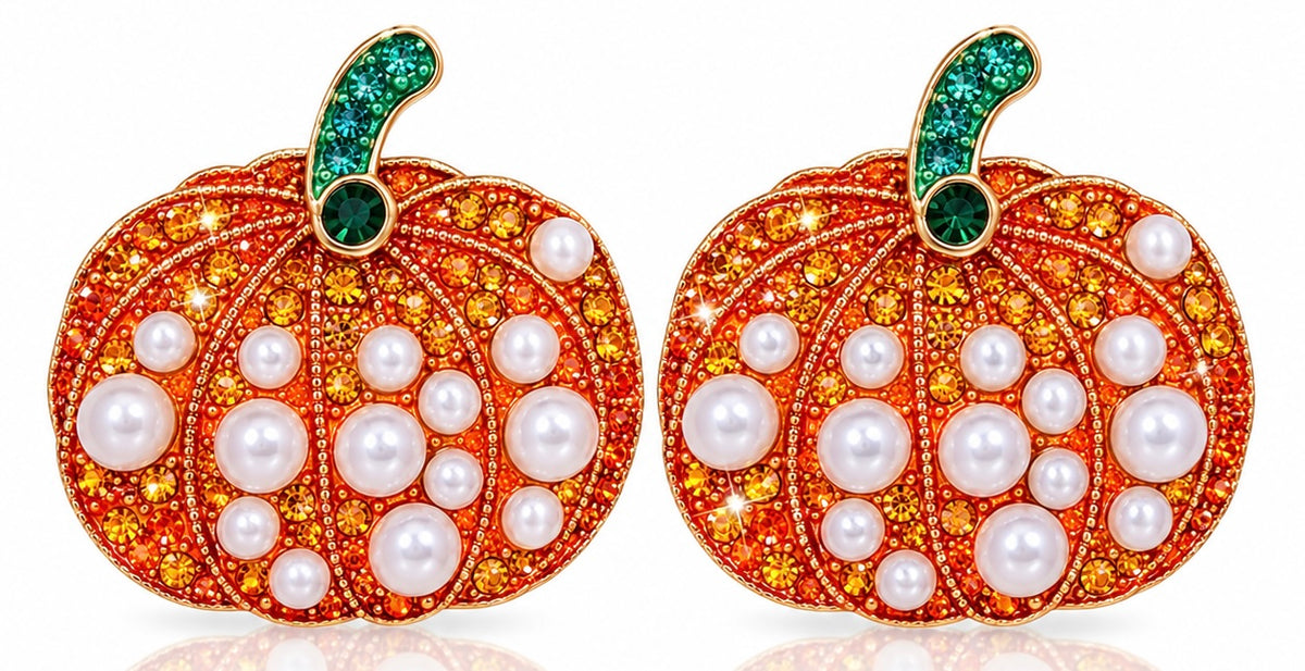 A pair of pumpkin-shaped earrings featuring orange pavé settings with white pearls, gold-toned metal outlines, and green crystal-studded stems, shown on a white background.