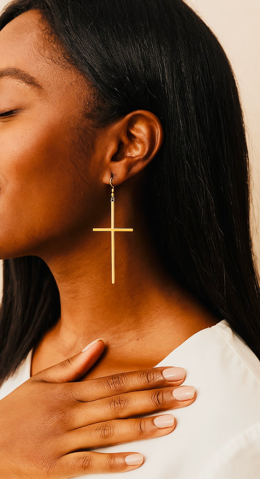 Woman wearing a gold cross earring with a neutral background