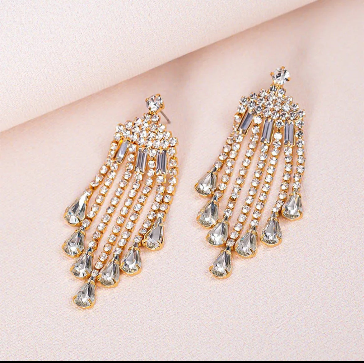 Pair of gold and crystal chandelier earrings on a light pink background