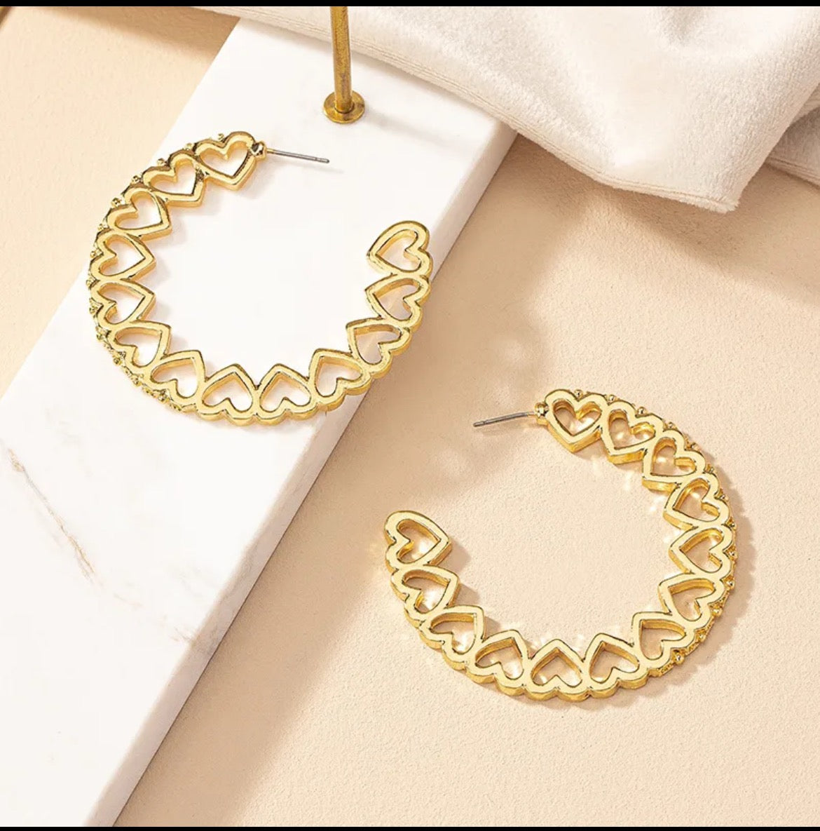 Gold hoop earrings with heart designs on a beige surface