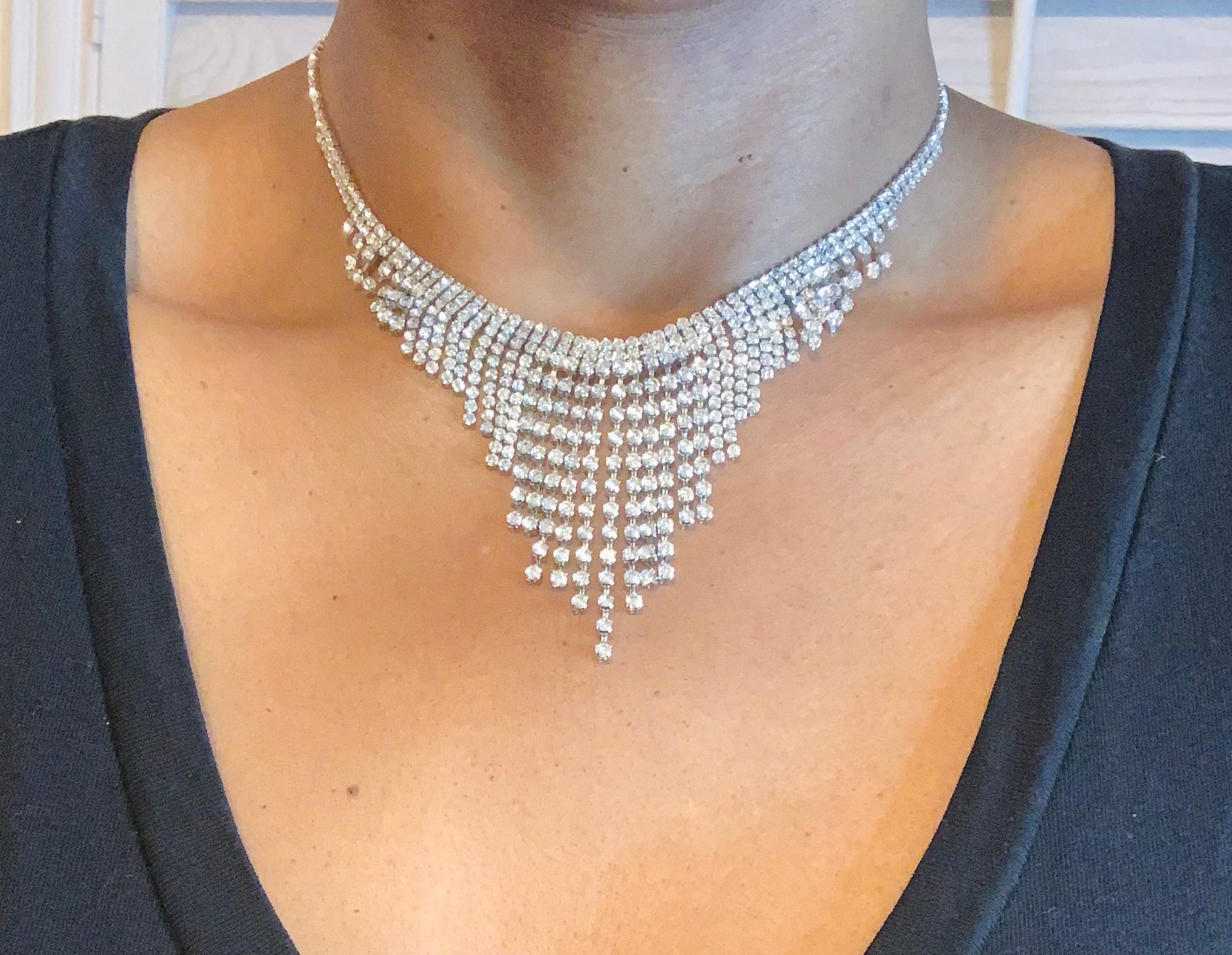 Silver necklace with dangling beads worn by a person against a neutral background