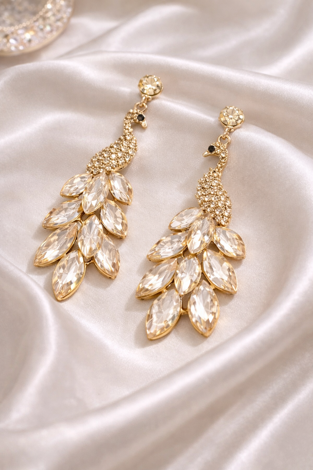 Gold and crystal earrings on a white satin surface