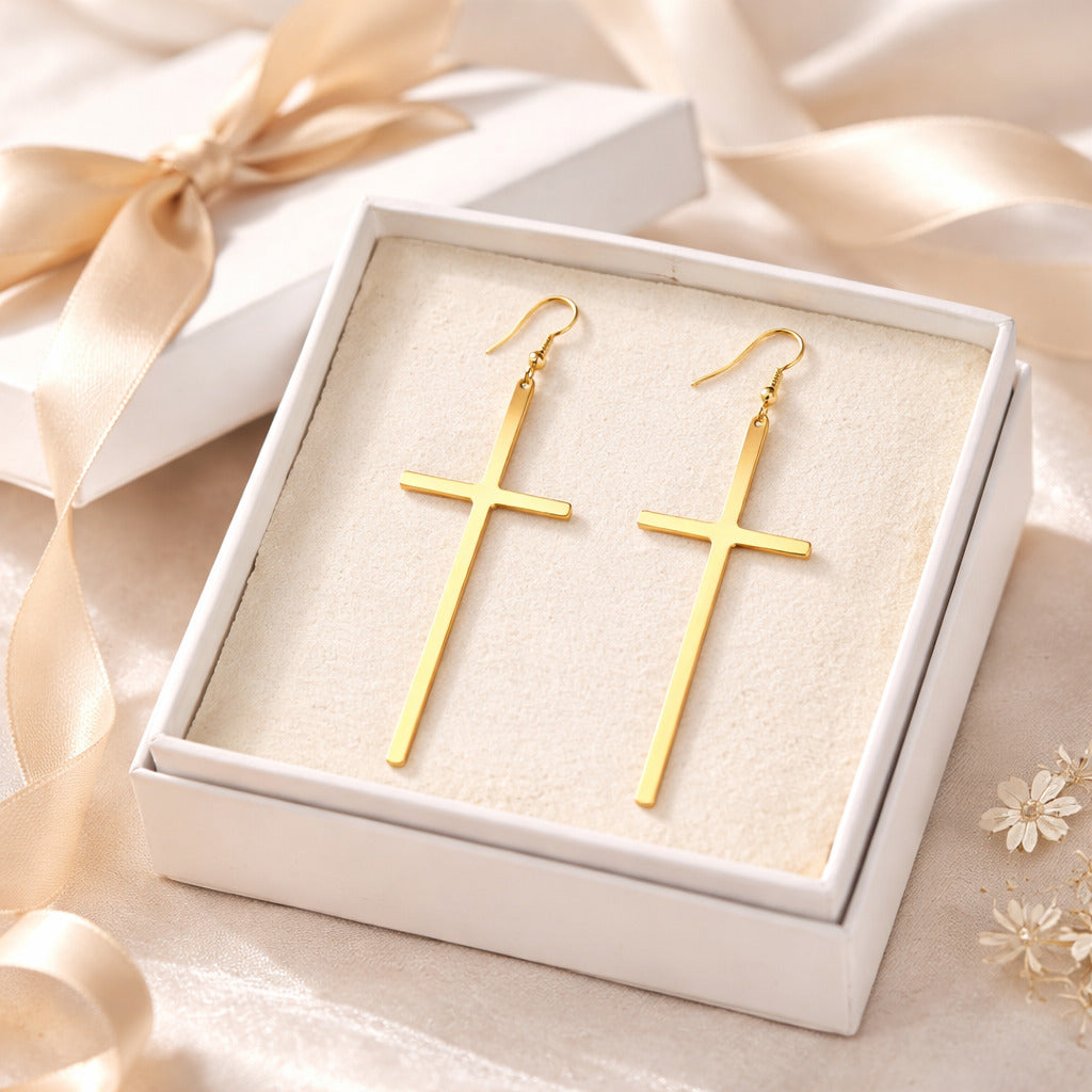Gold cross earrings in a white box with ribbons and flowers on a soft background
