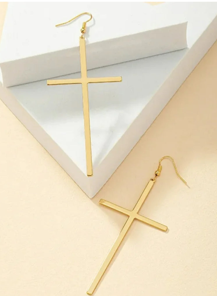 Gold cross-shaped earrings on a beige surface with a white box in the background