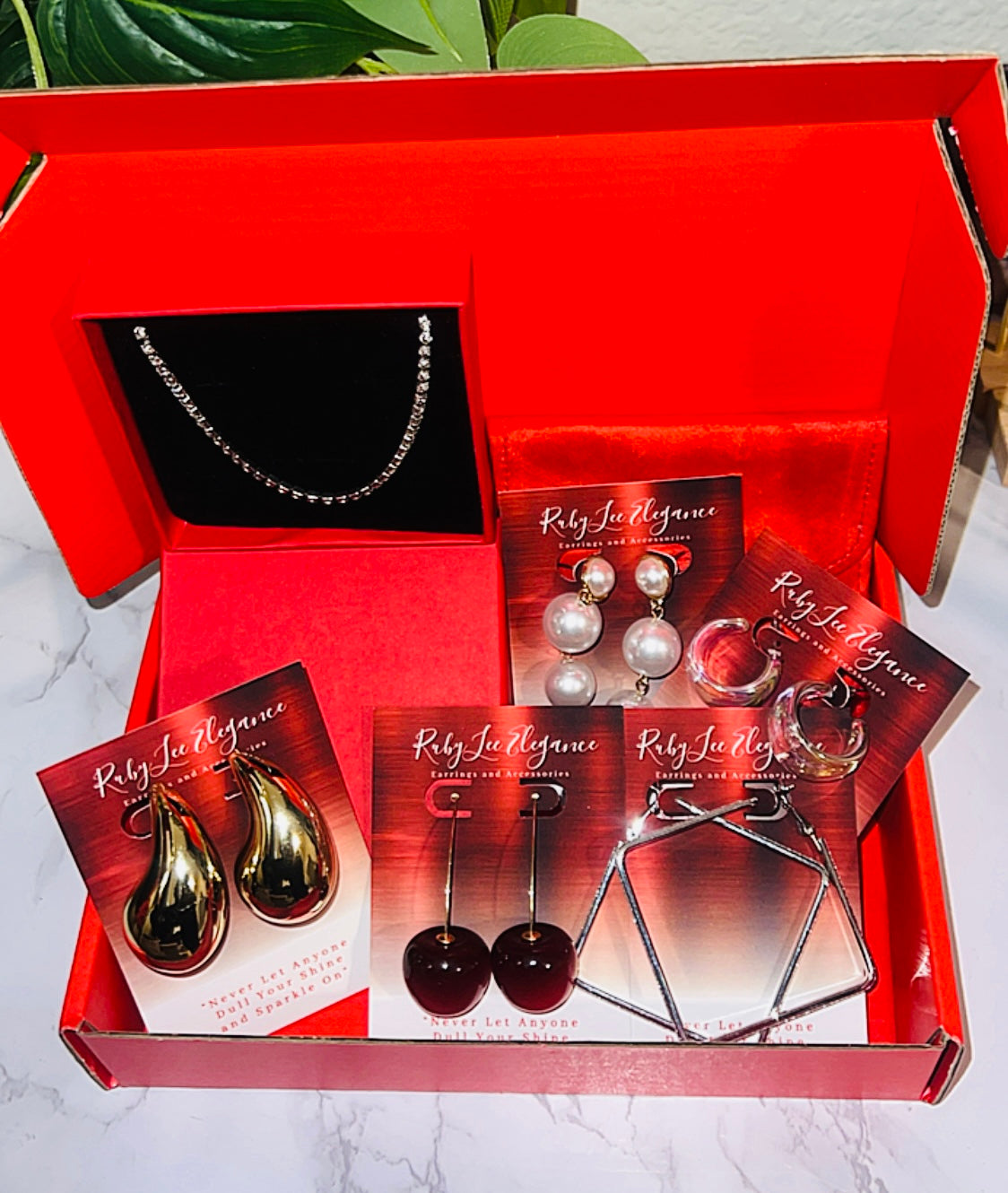 Jewelry set with earrings and a necklace in a red box on a marble surface.