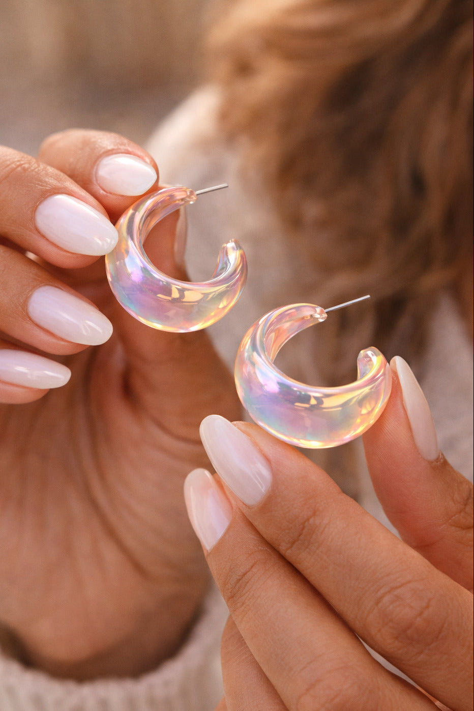 Holographic hoop earrings held by a person with light nail polish.