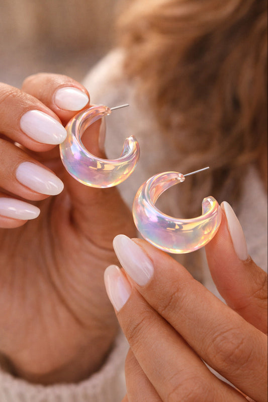 Holographic hoop earrings held by a person with light nail polish.