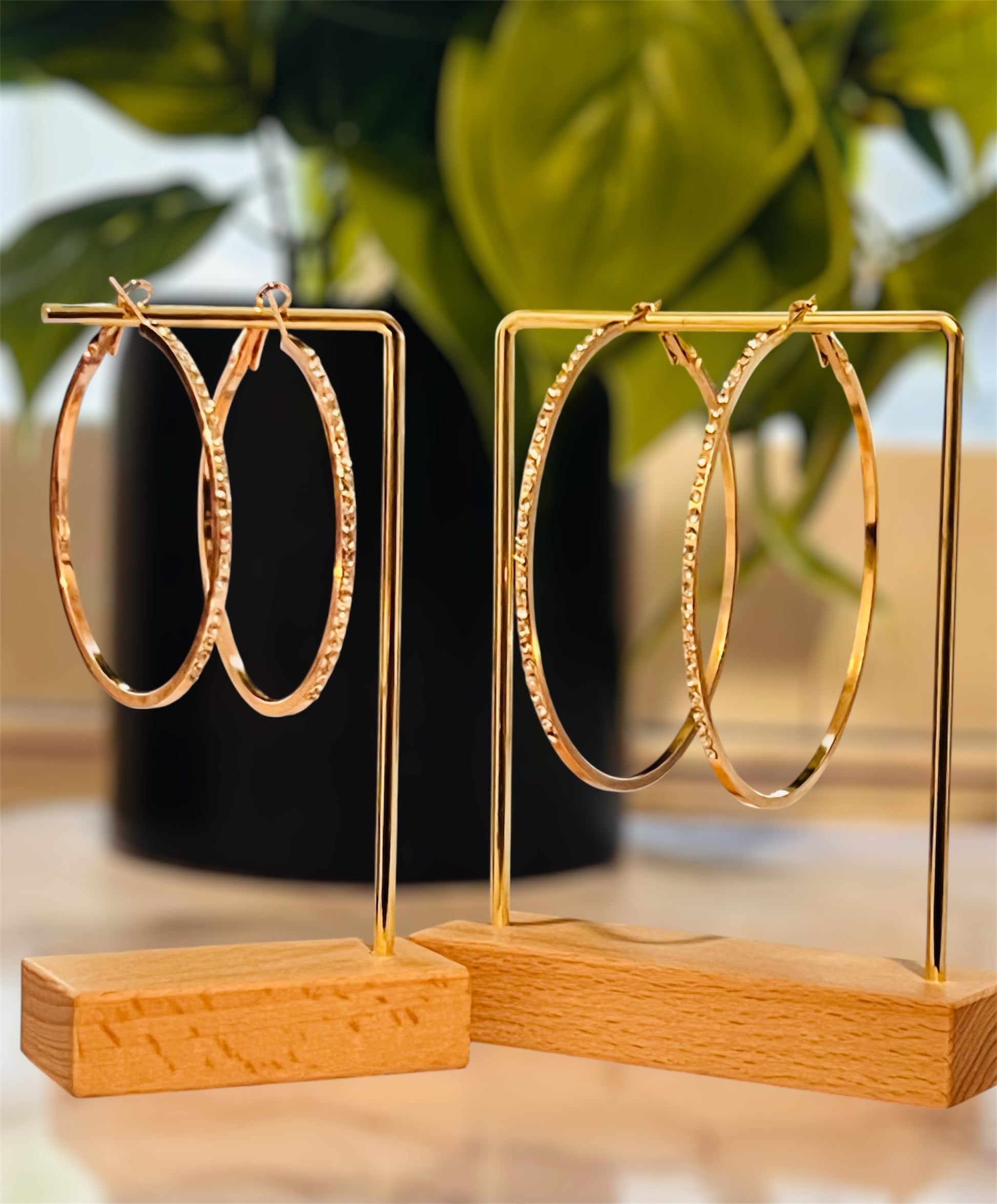 Gold hoop earrings on a wooden stand with a blurred green plant in the background