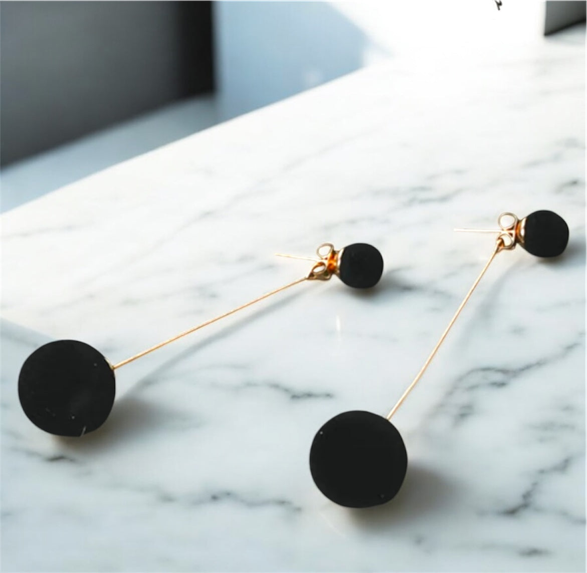 Black earrings with gold hooks on a marble surface