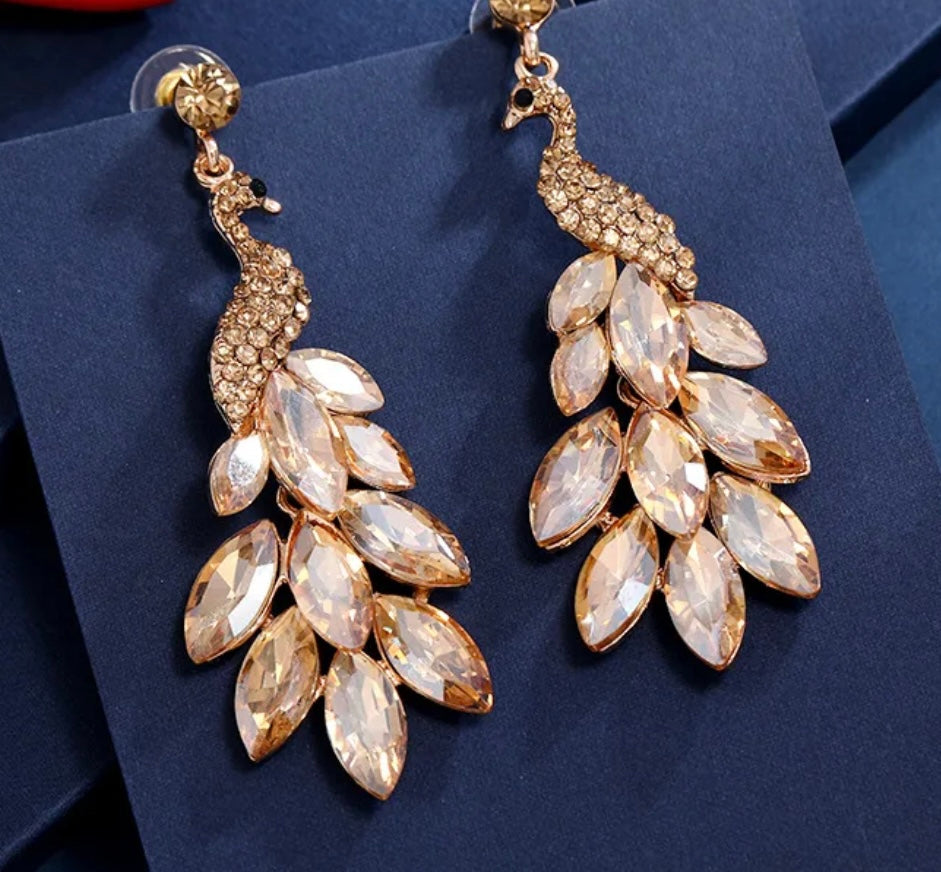 Gold peacock-shaped earrings with crystal-like stones on a dark blue background