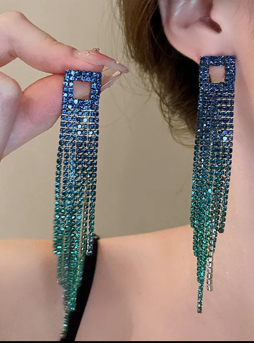 Close-up of a person wearing long, blue beaded earrings against a neutral background.