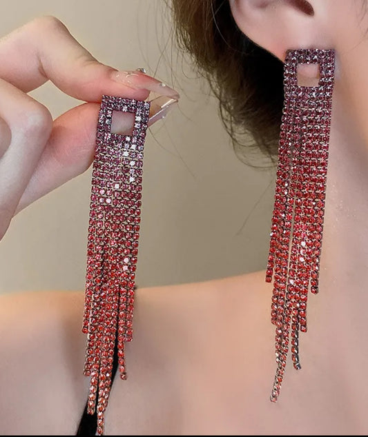 Close-up of a person wearing long, dangling earrings with red gemstones.