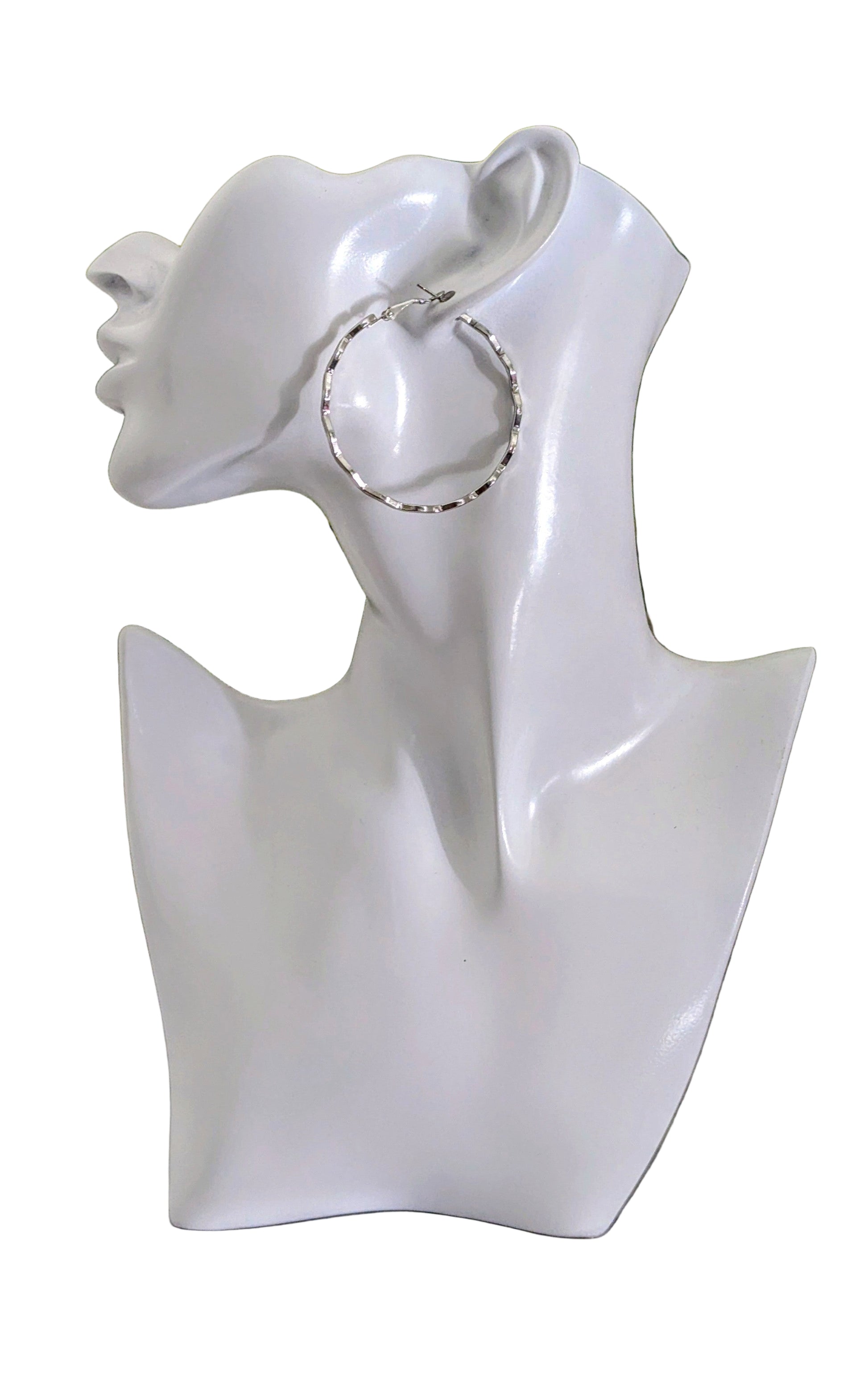 White bust with a silver hoop earring on a marble surface with greenery in the background