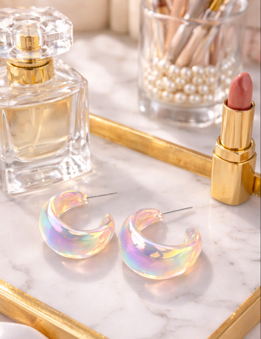 Iridescent hoop earrings on a marble tray with a perfume bottle and lipstick.