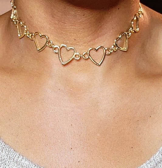 A gold-colored choker necklace with heart-shaped links, worn around the neck.