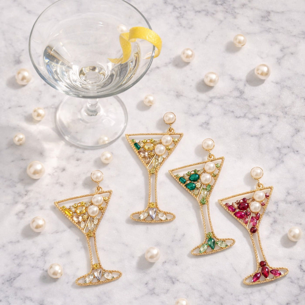 Martini glass-shaped earrings with gemstones on a marble surface with pearls.