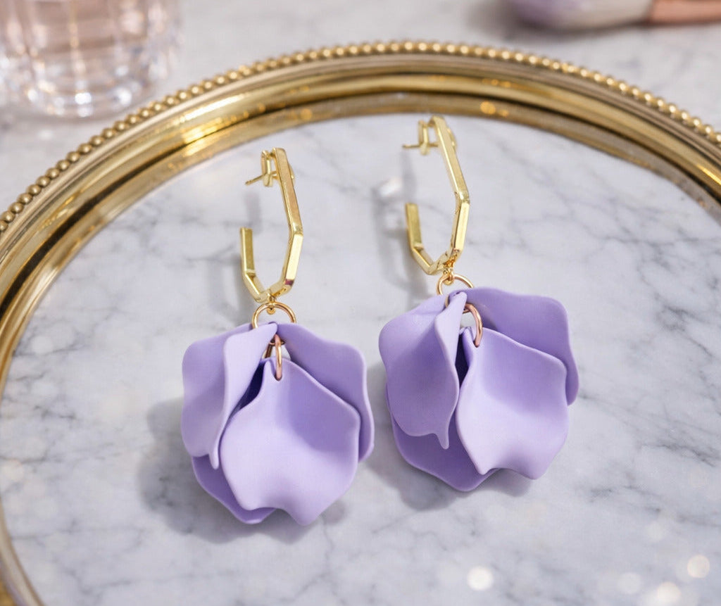 Purple flower-shaped earrings on a marble surface with a gold frame.