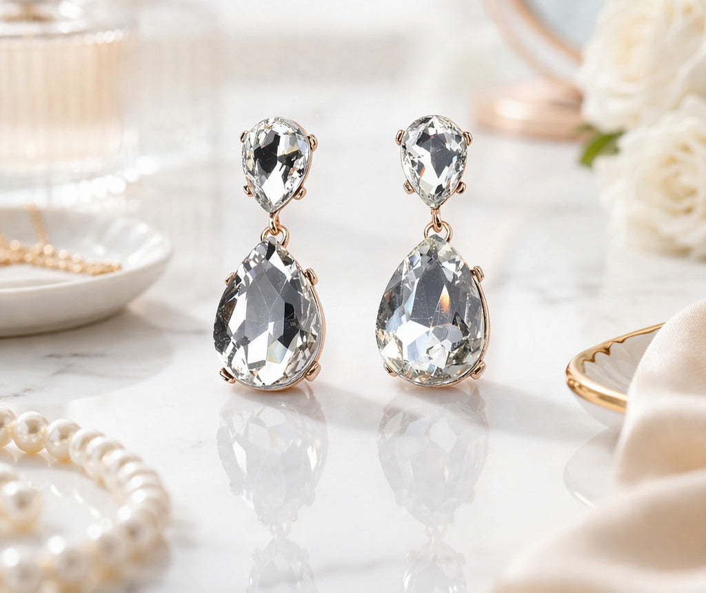 Pair of crystal earrings on a marble surface with flowers and jewelry in the background