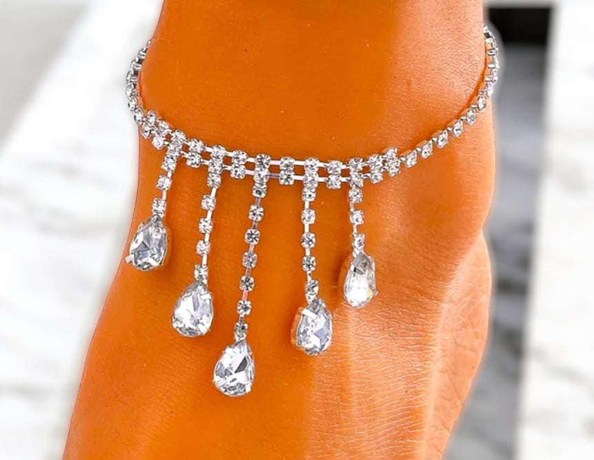 Silver anklet with dangling crystals on a person's ankle against a blurred background