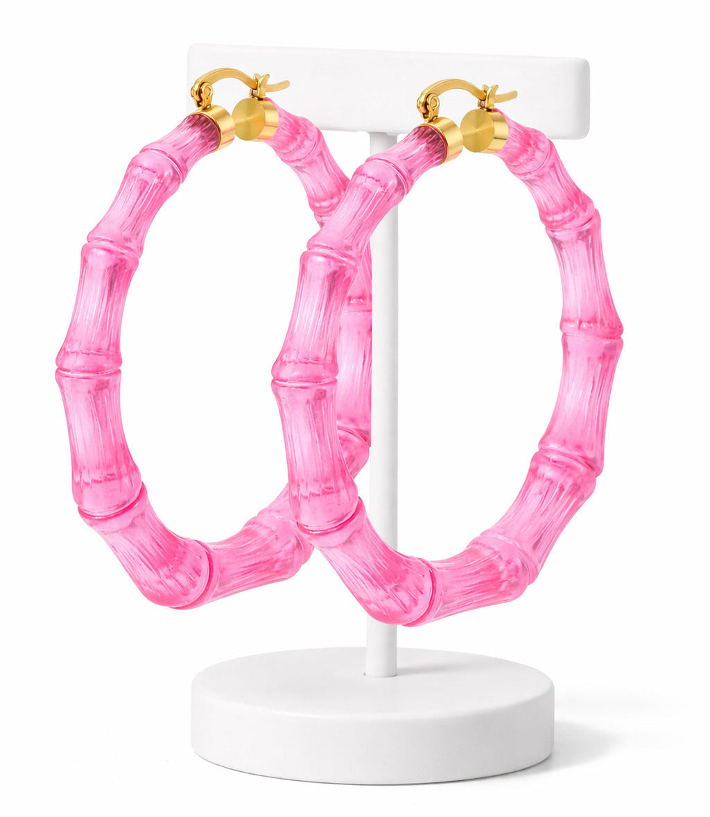Pink hoop earrings with gold accents on a white stand against a white background