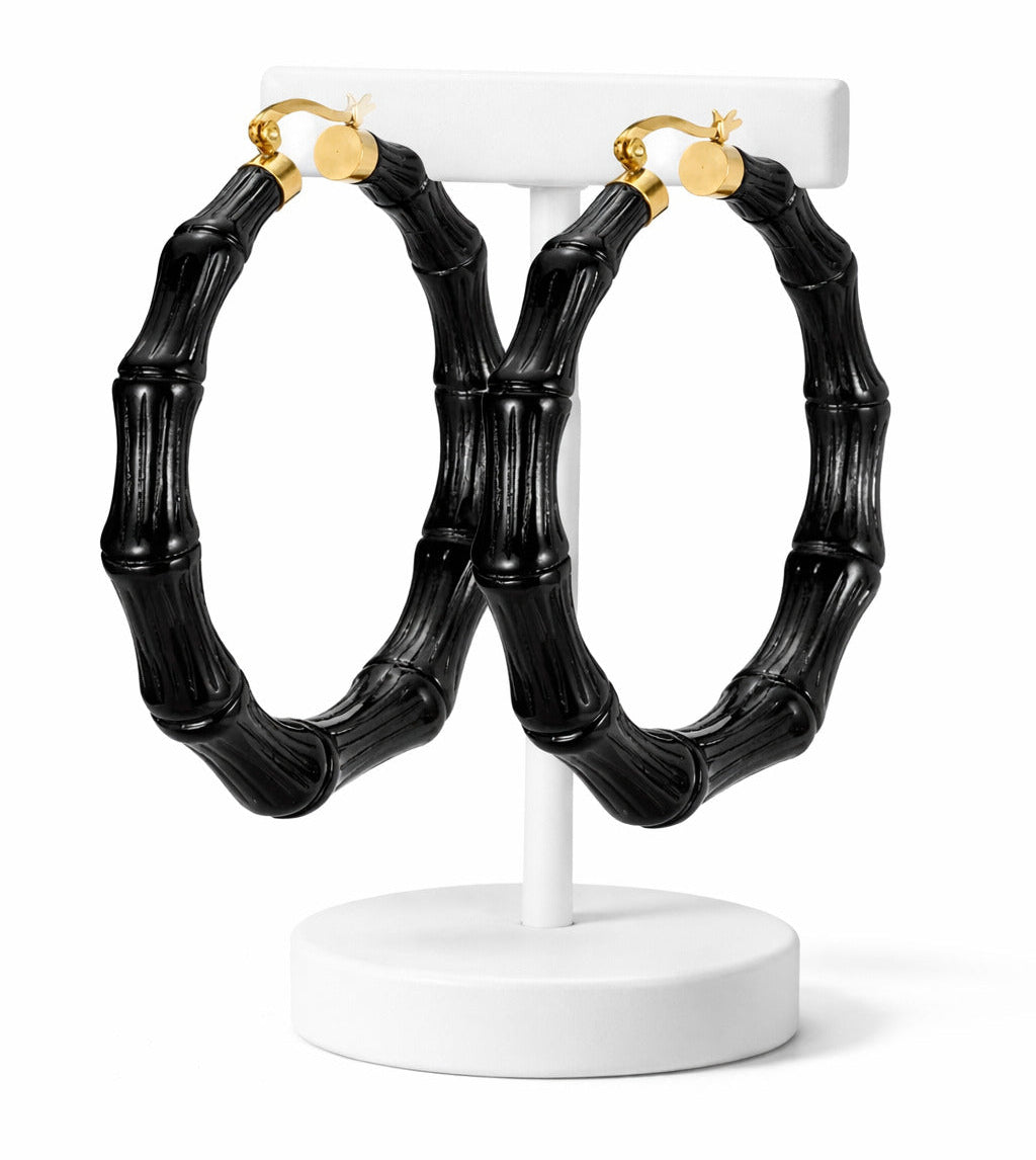 Black bamboo hoop earrings on a white stand with gold accents.