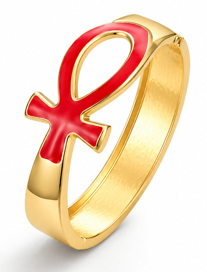 A gold-plated bracelet featuring a red enamel Ankh symbol on the front, set against a clean white background.