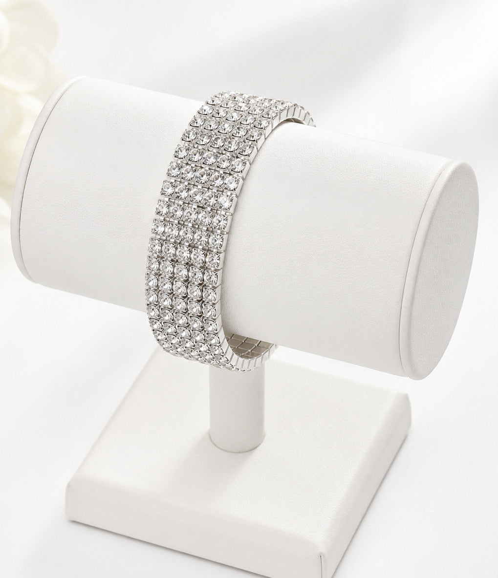 A sparkling silver-toned double-row rhinestone bracelet displayed on a white cylindrical jewelry stand against a bright white background.