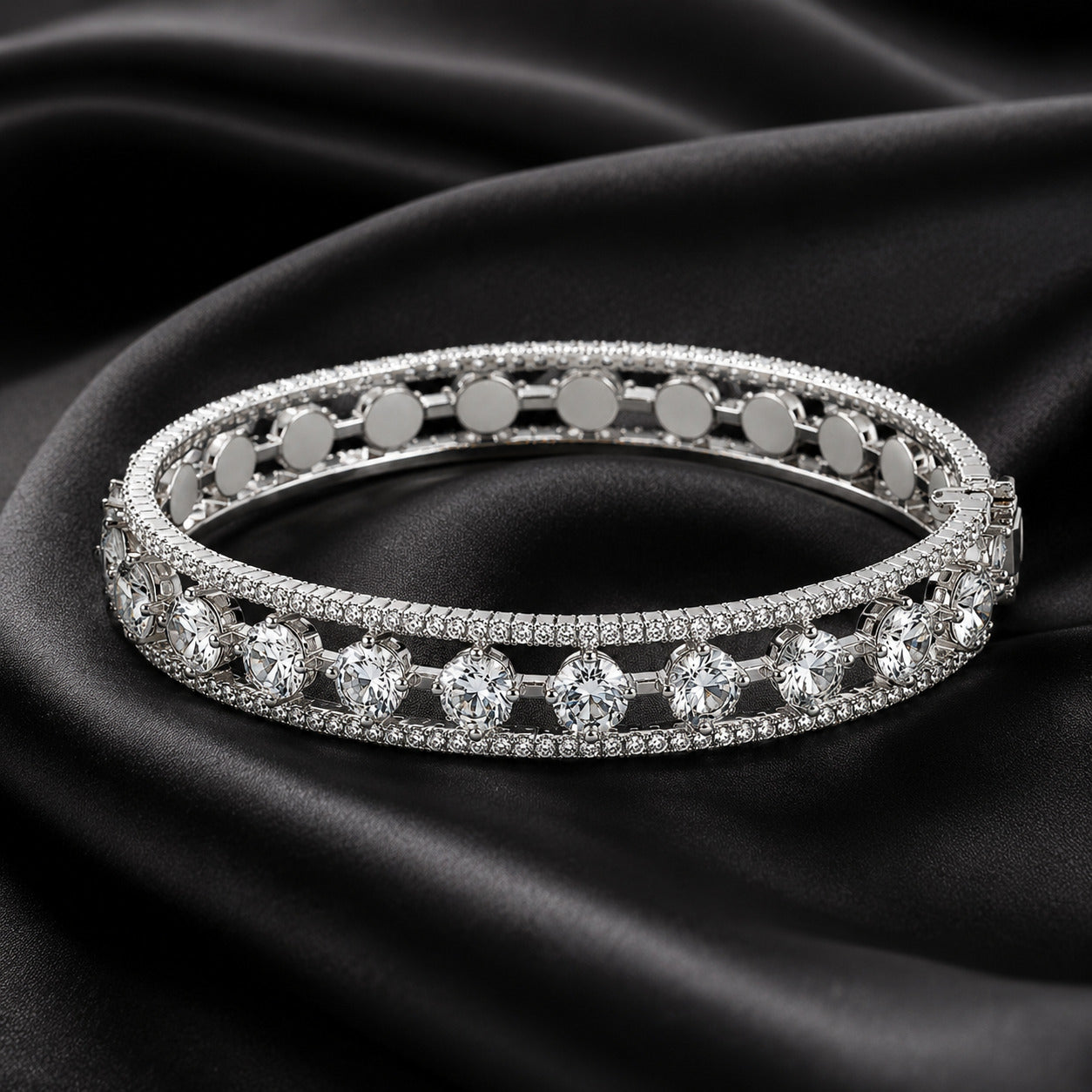 A double-row tennis-style bangle bracelet with round-cut clear stones and pavé-set silver-toned metal, displayed on draped black satin fabric.